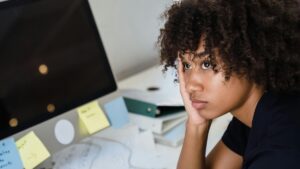 Erschöpfte Frau stützt Kopf auf die Hand vor Computer