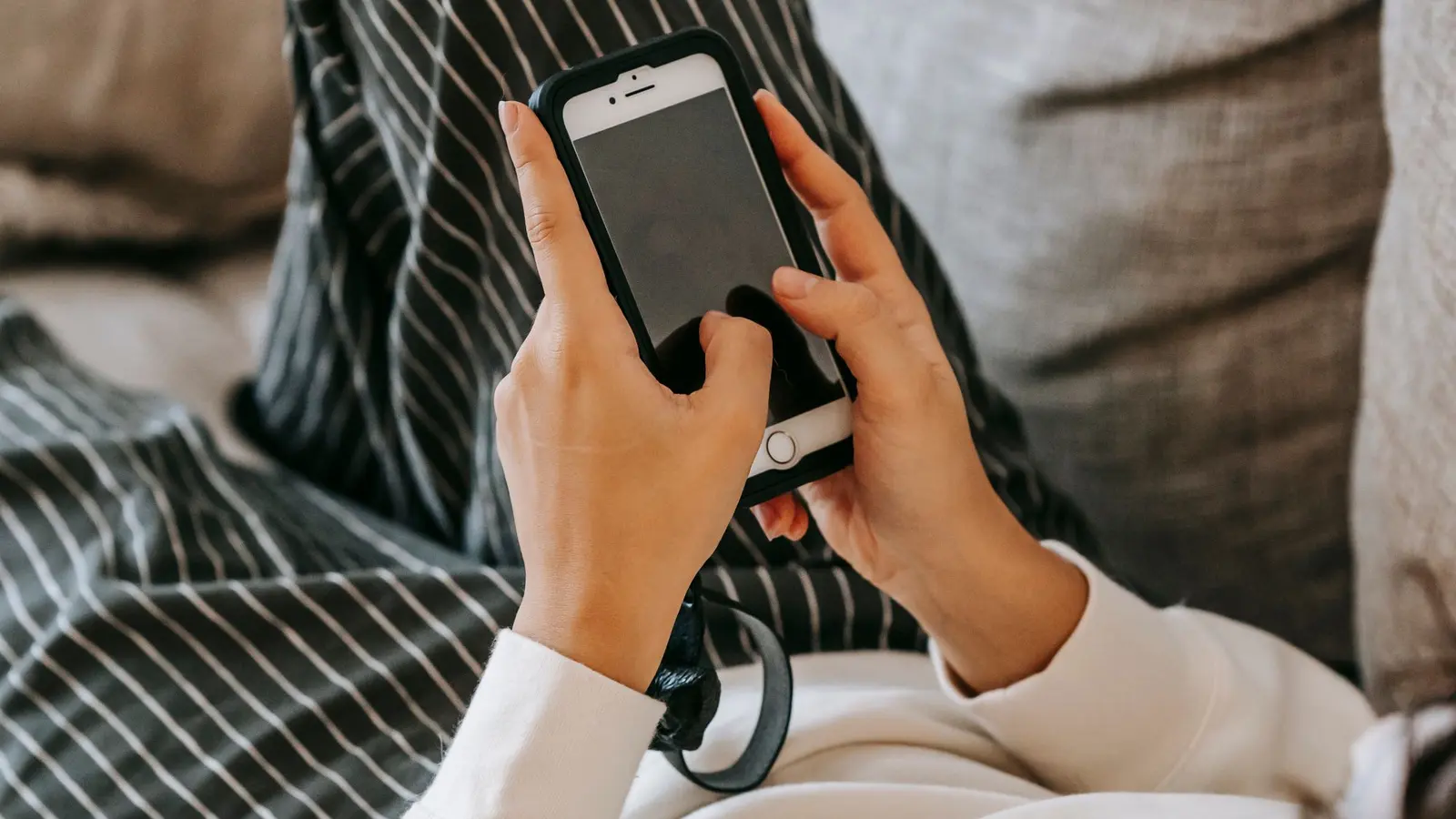 Hände halten ein Smartphone auf einem Sofa.