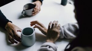 Drei Menschen im ruhigen Gespräch mit Kaffeetassen an einem Tisch