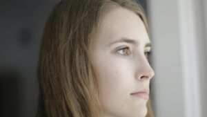 Junge Frau schaut nachdenklich aus dem Fenster